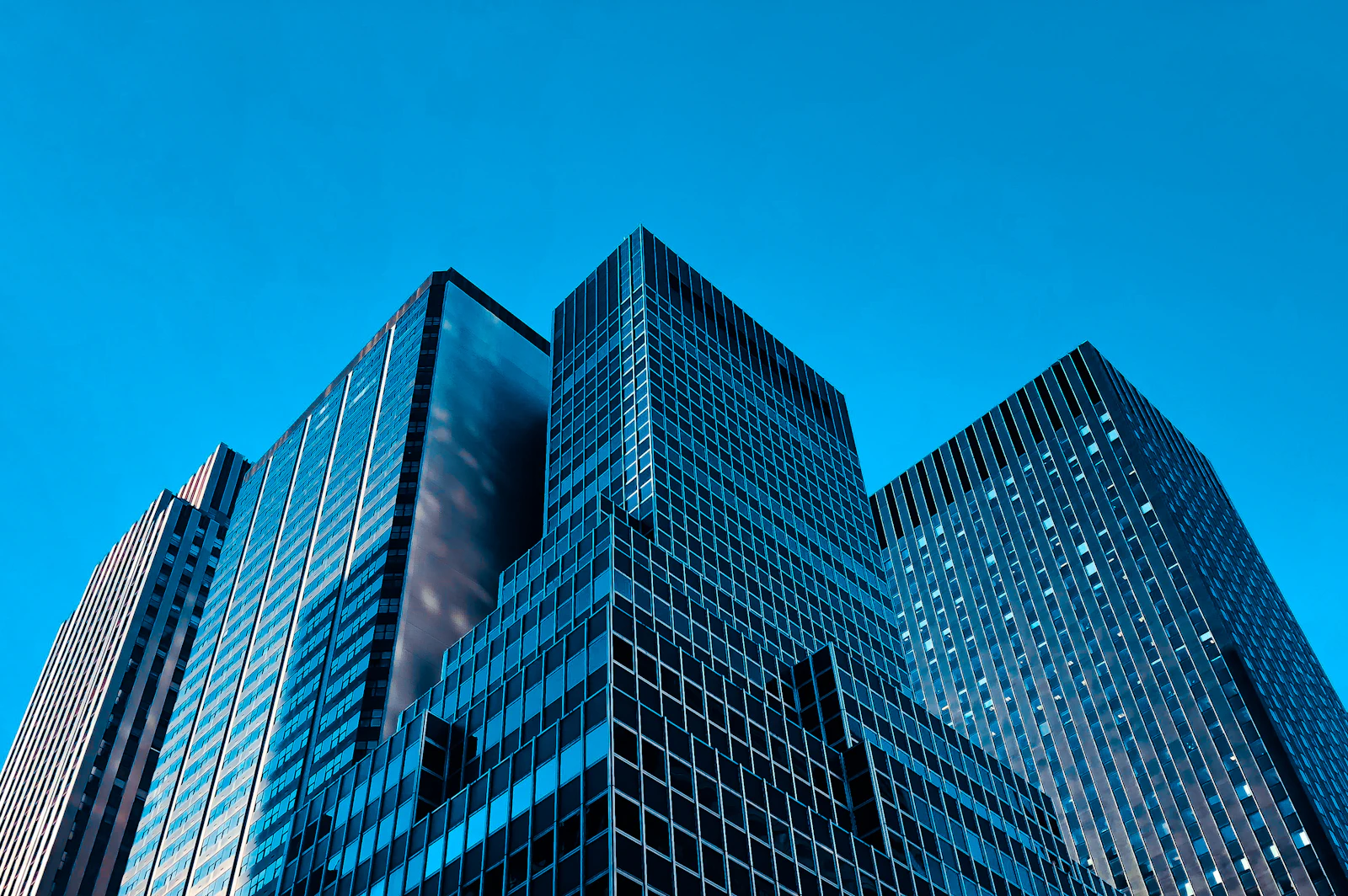 Torres corporativas de vidro vistas de baixo, céu azul ao fundo